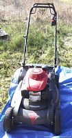 Front view of mower on blue tarp in grass with handle upright