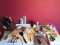 Full view of kitchen utensils on table including wooden knife block with knives, cooking utensils, kitchen tools like spatulas, salt and pepper grinders, and measuring spoons.