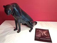 Full view of cast bronze cheetah sculpture on white cloth against red background