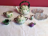 Wide view showing entire shamrock-themed tea set with glass plates and small porcelain pitchers arranged on white surface.
