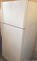 Front view of white Whirlpool refrigerator with top freezer and curved handle.