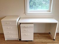 White minimalist desk with rolling file cabinet and dresser beside it under a window, showing size and proportions.