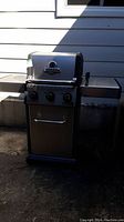 Full left-side angled view of the Broil King Baron propane BBQ grill, showing side shelf and wheels underneath.
