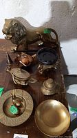 Overall lot showing brass lion figurine, incense holder, small brass dish, ducks and various small brass decor pieces, arranged on wooden table.