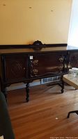 Front view of wooden sideboard buffet with two center drawers, two cabinet doors on either side, decorative brass hardware, and carved wood detail on top