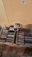Two plastic bins filled with a variety of music CDs, AM/FM radio and a small digital camera on top