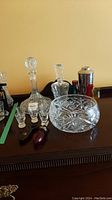 Wide view of entire lot showing crystal decanters, bowl, liqueur glasses, drink shaker, stopper, and opener on wooden surface.