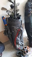 Photo showing black golf bag with golf clubs including irons, driver, woods, and putters, along with a black umbrella attached
