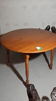 Front view of round pinewood dining table showing table top surface with some scratches and four turned legs.
