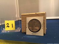 1967 Canadian silver dollar coin in white cardboard flip holder with textured box behind, showing the reverse side with design and year 1967.