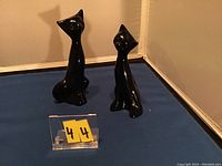 Photo showing two black glass cat figurines sitting side by side on a blue surface with a reflective background.
