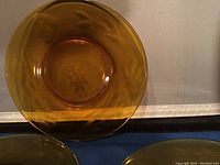 Top-down view of an amber glass plate showcasing the 3 petal bud cutting floral design etched into its translucent surface.