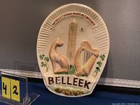 Front view of Belleek ceramic wall plaque showing raised dog, harp, tower, shamrocks, and Belleek text.