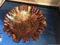 Photo of an amethyst carnival glass bowl with embossed thistle pattern and ruffled edge placed against a dark background