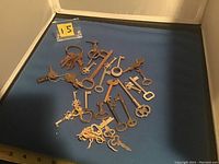 Photo of approximately 26 mixed vintage and modern keys arranged on a blue surface for cataloging.