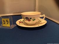 Front angled view of the porcelain cup on its matching saucer displaying floral patterns and burgundy rim detail.