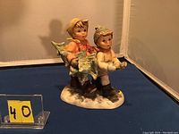 Side and front view of Goebel porcelain figurine of children carrying a Christmas tree on a snowy base.