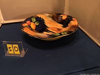 Photo showing the full view of the scalloped bowl with colorful autumn fruit and leaf pattern on a gradient brown and blue background.