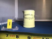 Front and side view of a yellow ceramic creamer marked 'NANKING TAVERN' with ruler providing size reference around 3 to 4 inches tall.