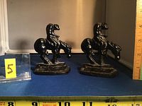 Two black metal horse and rider bookends shown with a ruler for size reference.