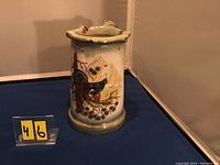 Front side of ceramic puzzle jug showing game bird on natural landscape and holes for puzzle function.