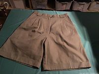 Image showing front view of khaki ladies shorts laid flat on green surface, highlighting pleated front and belt loops.