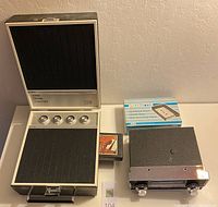 Two 8-track players on table: Elgin portable player with open lid and control knobs; Borg Warner car stereo with removable cartridge and box.
