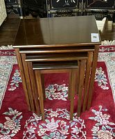 Front view of the four nested tables stacked inside each other on a floral carpet, showing their rectangular tops and wooden legs.