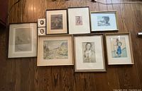 Overview of nine framed art pieces arranged on floor showing varied sizes and subjects