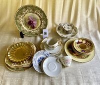Overview of set showing various plates, cups, saucers, and place card holders arranged on cloth.