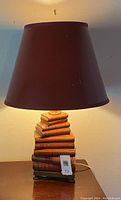 Full view of lamp with lit brown lampshade and stacked vintage books base