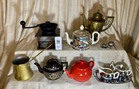 Full overview of the coffee and tea set showing 3 teapots, coffee grinder, brass pitcher, cream and sugar set, 2 Turkish coffee pots, and 2 tea strainers.