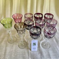 Eleven cut crystal stemware goblets grouped showing color and cut patterns including cranberry and tulip-topped glasses.