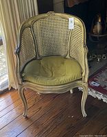 Front view of French Louis XV style caned bergere chair with green velvet cushion on wooden floor near window.