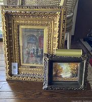 Overview of both gilt framed prints and clip-on art light on hardwood floor
