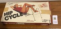 Photo of boxed vintage Hip Cycle exercise machine with illustrated woman exercising on front of box and condition showing edge wear and taped corners.