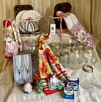 Various kitchen items on beige fabric backdrop including mason jars, aprons, champagne flutes, metal plate rack, muffin pans