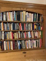 Wooden bookshelf front view showing three upper shelves densely packed with books
