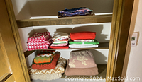 Folding linens in a wooden closet shelf, showing stacks of folded picnic napkins, fabric pieces, and blankets with various colors and patterns.