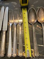 Two knives, three forks, two spoons laid next to measuring tape showing approximate lengths.