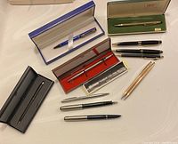 Photo showing full lot of pens displayed on a white surface, including boxes and various pen styles.