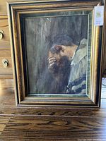 Full view of framed oil painting depicting a rabbi with head in hand in a dark background.