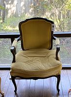 Frontal view of yellow velvet upholstered fauteuil arm chair showing seat cushion and walnut frame with carved detailing.