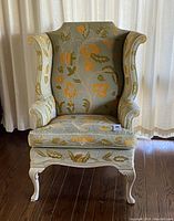 Front view of vintage wingback chair with floral crewel upholstery and painted wooden frame