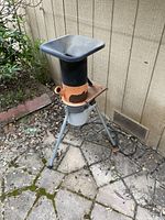 Full view of the Steinmax 1800 chipper shredder showing the orange and black body supported on metal legs outdoors against a wooden wall.