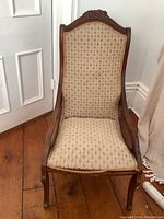 Front view of the antique chair showing patterned upholstery and carved wooden frame with scratches visible on legs and arms.