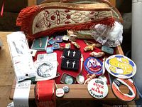 Overview of the lot showing ceremonial sashes, button pins, badges, spoons, display case, and various small collectibles spread on a wooden surface.