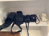 Three film cameras and two carry cases on white shelf. Cameras include black Pentax 105 Super, white Lomography Fisheye, and black Chinon 35 FA Super.