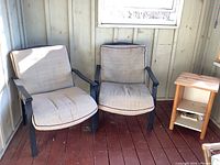 Metal framed patio chairs with beige fabric cushions and small wooden table in a sunlit room, showing overall condition and setup.