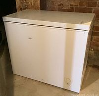 White rectangular Frigidaire chest freezer with visible rust spots on front and scratches on top surface in basement setting.